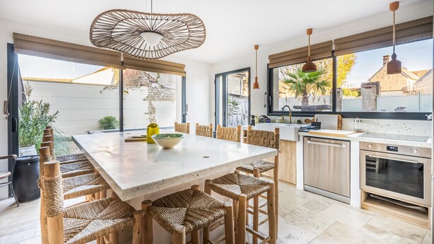 Una cocina moderna con una isla grande, sillas de mimbre y una lámpara colgante.