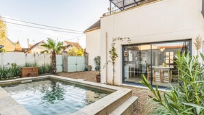 Una casa moderna con piscina, un ventanal de vidrio que da a un comedor, y un jardín con diversas plantas.