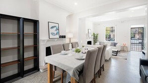 A dining area with a table set for four, a bookshelf, and a fireplace. - Darlinghurst Living | 5 Beds + Garage Parking (Darlinghurst)