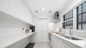 A narrow kitchen with white cabinetry, a black and white tiled floor, a window with blinds, and a sink with a faucet. - Darlinghurst Living | 5 Beds + Garage Parking (Darlinghurst)