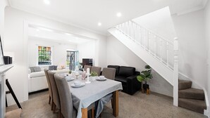 A modern living room with a dining area, a staircase, and a view of the outdoors. - Darlinghurst Living | 5 Beds + Garage Parking (Darlinghurst)