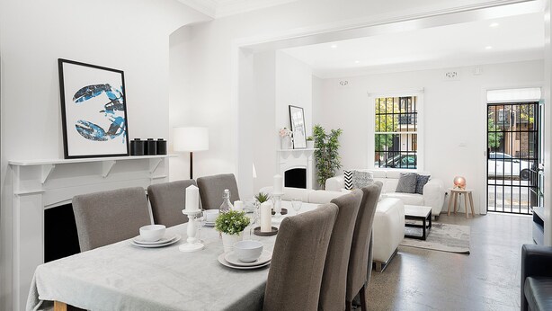 A modern dining area with a white table set for six, surrounded by grey upholstered chairs. A fireplace is visible in the background, and a large window with a view of the outside is present. - Darlinghurst Living | 5 Beds + Garage Parking (Darlinghurst)