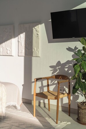 Een kamer met een bed, een houten stoel, een bloempot en een tv aan de muur.