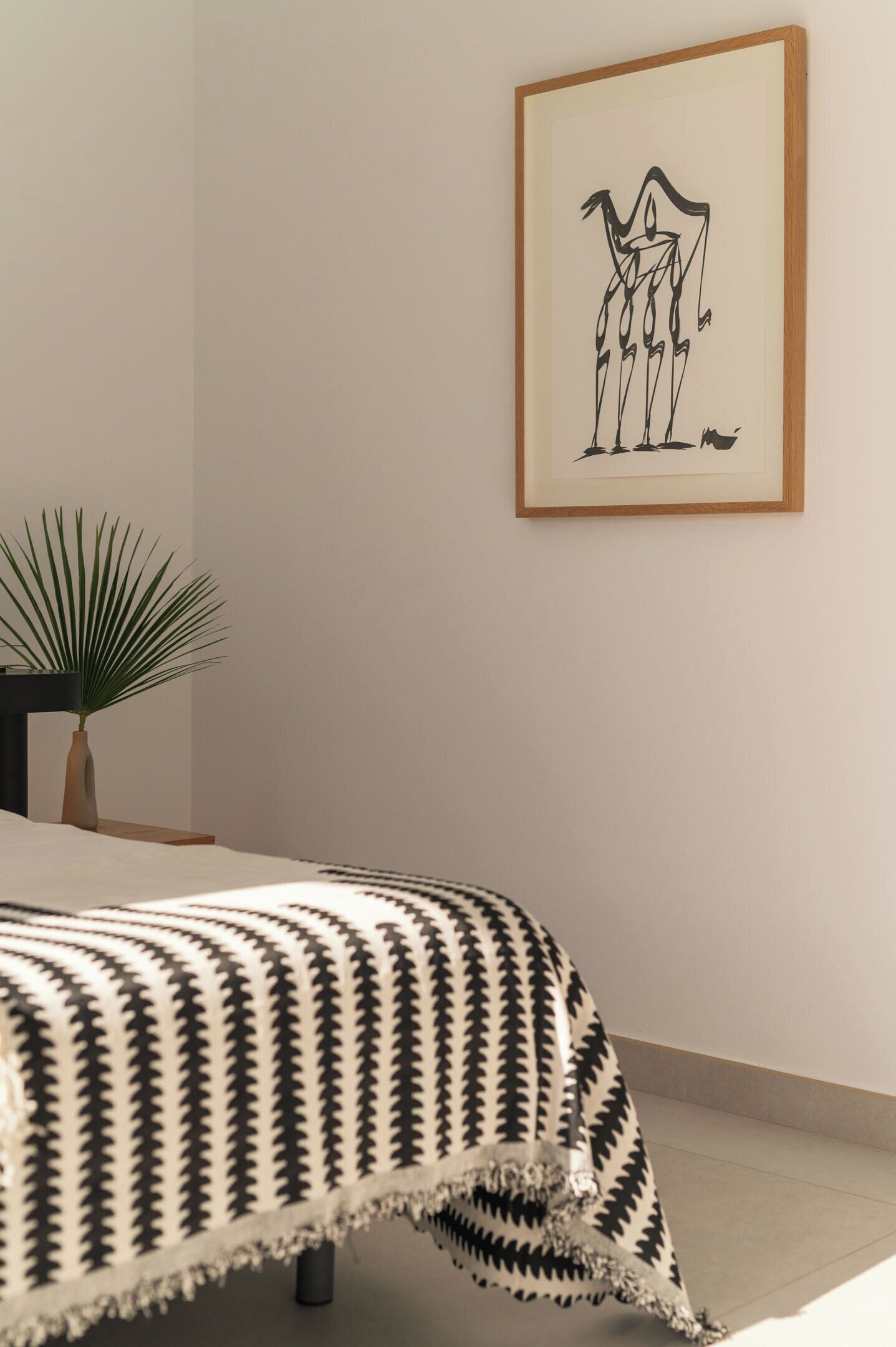 A bedroom with a bed, a framed artwork on the wall, and a potted plant.