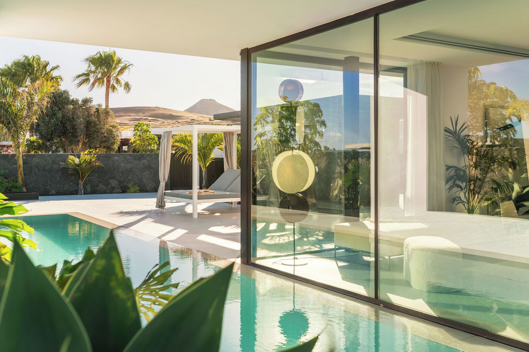 A modern pool area with glass walls, a lounge chair, and a view of a mountain.