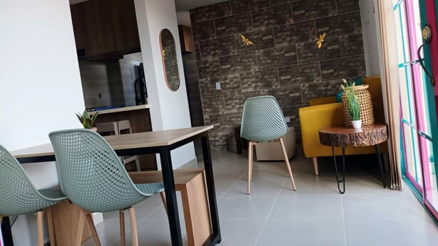 A modern kitchen with dark tiles, a dining area with green chairs, and a yellow sofa. - Jardines del Lago  (Guatapé)
