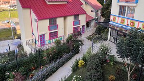 A multi-story building with a red roof and balconies, surrounded by greenery and a mountainous backdrop. - Jardines del Lago  (Guatapé)