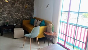 A modern living room with a yellow sofa, a patterned chair, a small side table with a plant, and a large window with a view of a pink railing. - Jardines del Lago  (Guatapé)
