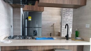 A modern kitchen with wooden cabinets, a stainless steel refrigerator, a gas stove, and two bar stools. - Jardines del Lago  (Guatapé)
