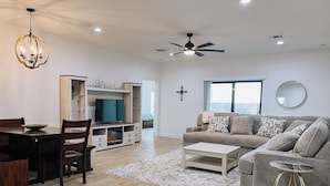 A modern living room with a dining area, a ceiling fan, a flat-screen TV, and a large window. - New build! Pool | 3bd | 2ba | Sleeps 7 | Views (Fort Mohave)