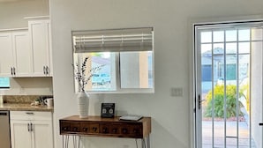 A kitchen with white cabinets, a wooden console table, a vase with a plant, a welcome sign, and a sliding glass door leading to an outdoor area. - New build! Pool | 3bd | 2ba | Sleeps 7 | Views (Fort Mohave)