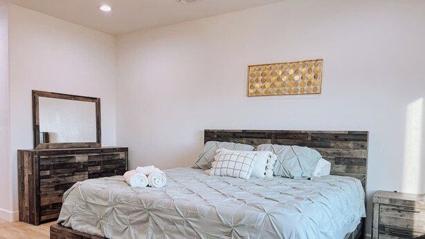 A bedroom with a wooden headboard, a bed with a quilted cover, a bedside table, and a wall-mounted artwork. - New build! Pool | 3bd | 2ba | Sleeps 7 | Views (Fort Mohave)