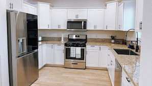 A modern kitchen with white cabinets, stainless steel appliances, and a granite countertop. - New build! Pool | 3bd | 2ba | Sleeps 7 | Views (Fort Mohave)