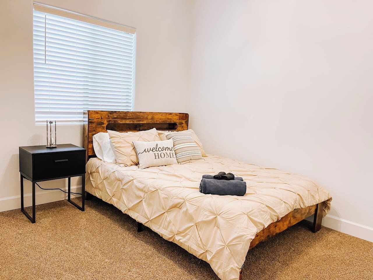 Una cama individual con cabecera de madera, una mesita de noche y una ventana con persianas.