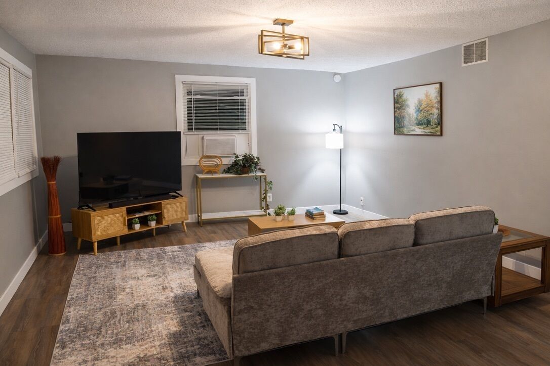 Ein modernes Wohnzimmer mit grauem Sofa, Flachbildfernseher, Holz-Couchtisch und Stehlampe.