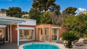 A swimming pool with a curved edge, a covered patio area, and a building with glass doors and a covered outdoor seating area.