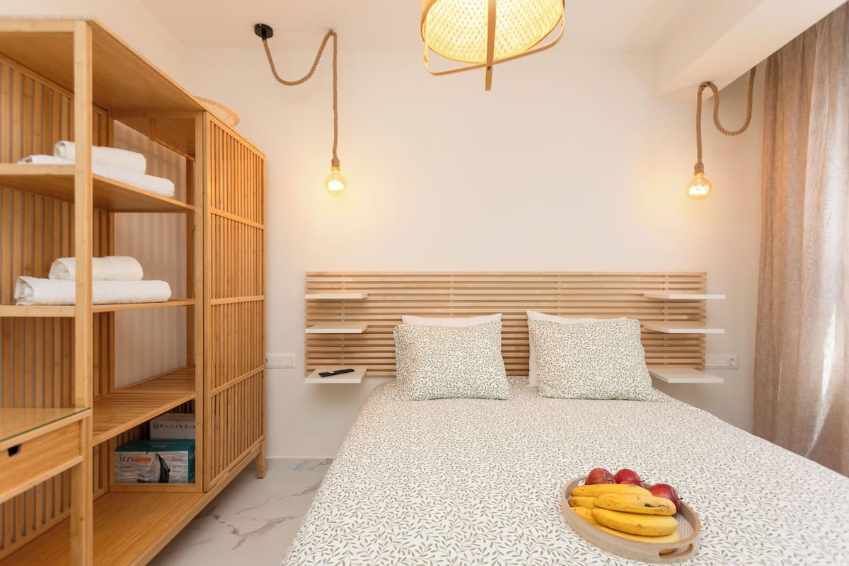 A modern bedroom with a wooden wardrobe, a bed with patterned bedding, and a fruit bowl on the bed.