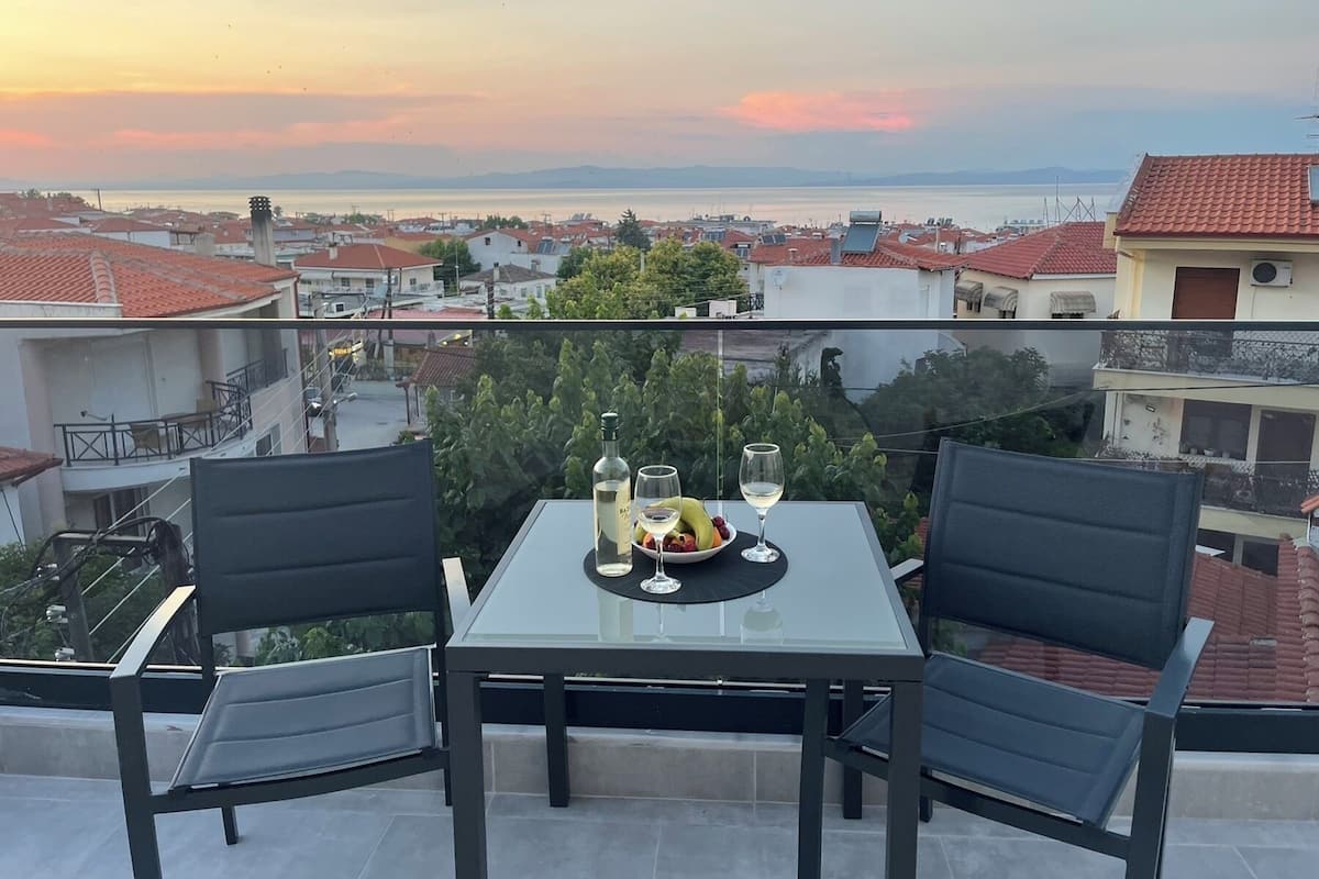 A table with two chairs on a balcony overlooking a cityscape at sunset.