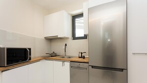Una cuina moderna amb armaris blancs, un frigorífic d'acer inoxidable, un microones, un rentaplats i un taulell de fusta.
