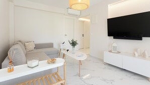 Un saló modern amb un sofà, una taula de dinar i un televisor fixat a la paret.