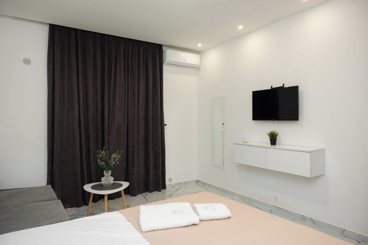 A modern hotel room with a bed, a small table with a plant, a TV mounted on the wall, and a white console unit.