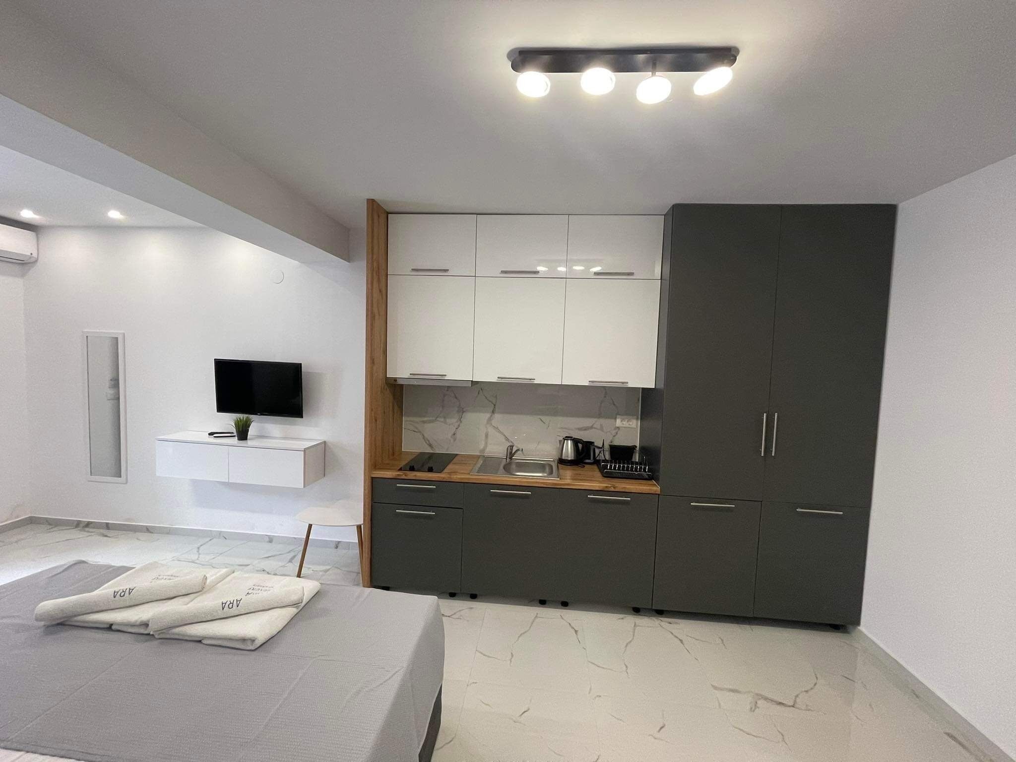 A modern bedroom with a bed, a TV, and a kitchenette with cabinets and a stove.