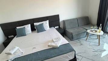 Una habitación de hotel moderna con una cama grande, un sofá gris y una pequeña mesa redonda con una botella y vasos.