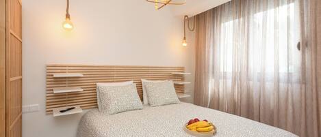 Um quarto moderno com cabeceira de madeira, cama com colcha estampada, mesa de cabeceira com tigela de frutas e luminária pendente.