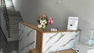 Un comptoir d’accueil au design en marbre, un comptoir en bois, un distributeur d’eau et un arrangement floral.