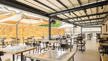 Un café en plein air avec des tables et des chaises, un mur en pierre et des parasols pour faire de l’ombre.