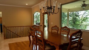 A dining area with a wooden table and chairs, a chandelier, and a view of trees through large windows. - Lakefront Hideaway - Boat Slip at Nearby Marina (Grove)