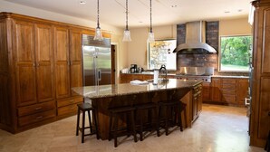 A spacious kitchen with wooden cabinets, a large island with bar stools, stainless steel appliances, and a stone backsplash. - Lakefront Hideaway - Boat Slip at Nearby Marina (Grove)