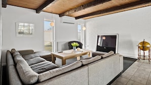 A modern living room with a wooden ceiling, a large sofa, a dining table, and a TV. - Stunning home in Blokhus with sauna (Blokhus)