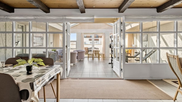 A spacious room with large windows, a dining area, and a view of the outside balcony. - Stunning home in Blokhus with sauna (Blokhus)