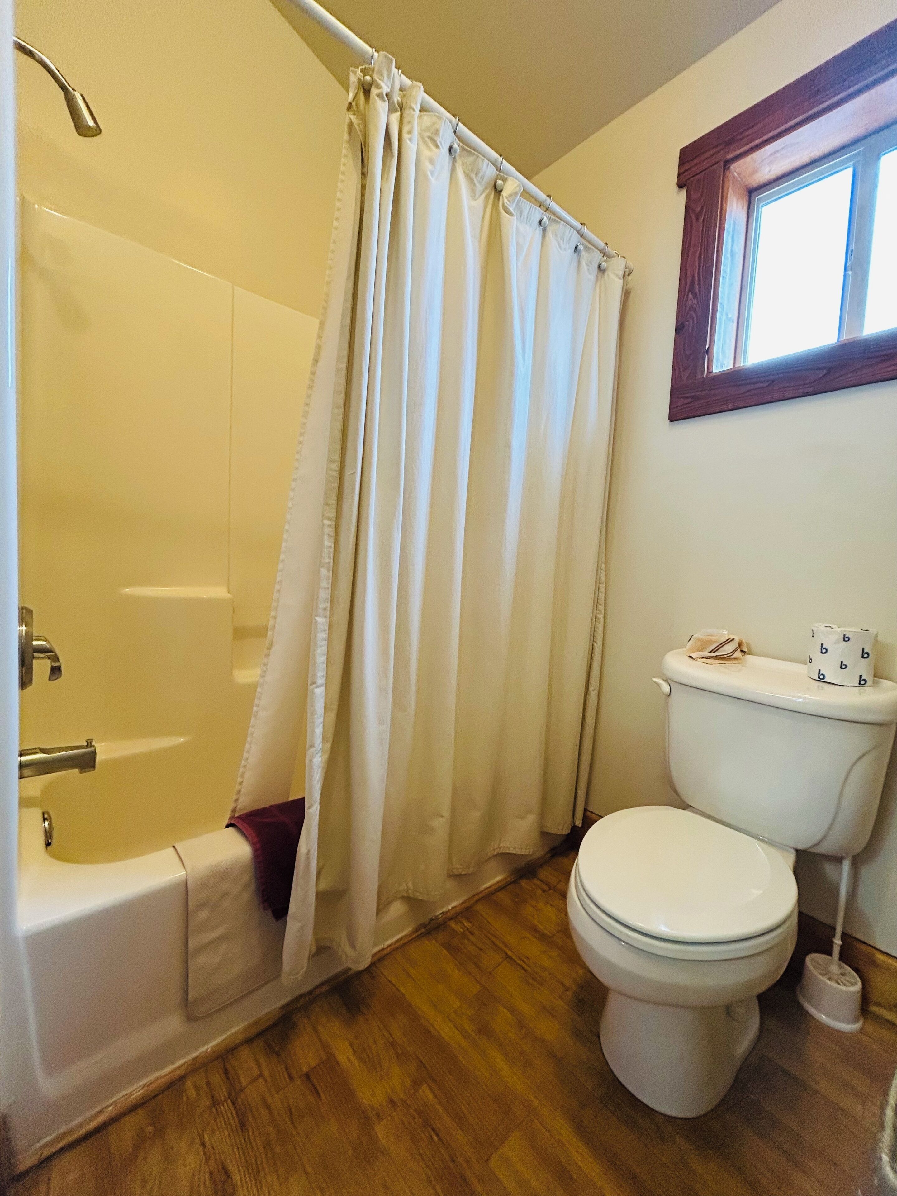 A bathroom with a bathtub, toilet, and a window above the toilet.