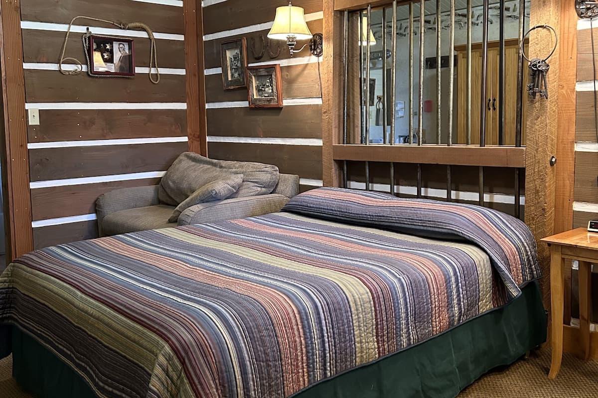 A room with a wooden slat wall, a bed with striped bedding, a small table, and a window with bars.