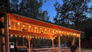 Un espace pique-nique extérieur abrité, agrémenté de guirlandes lumineuses, de tables de pique-nique et d’un barbecue.