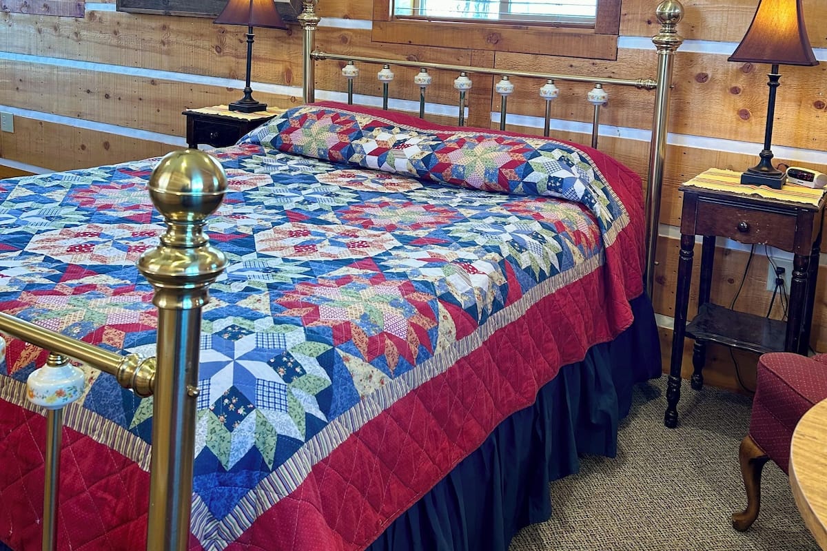 A wooden-paneled room with a large bed, a framed portrait, and a window with blinds.