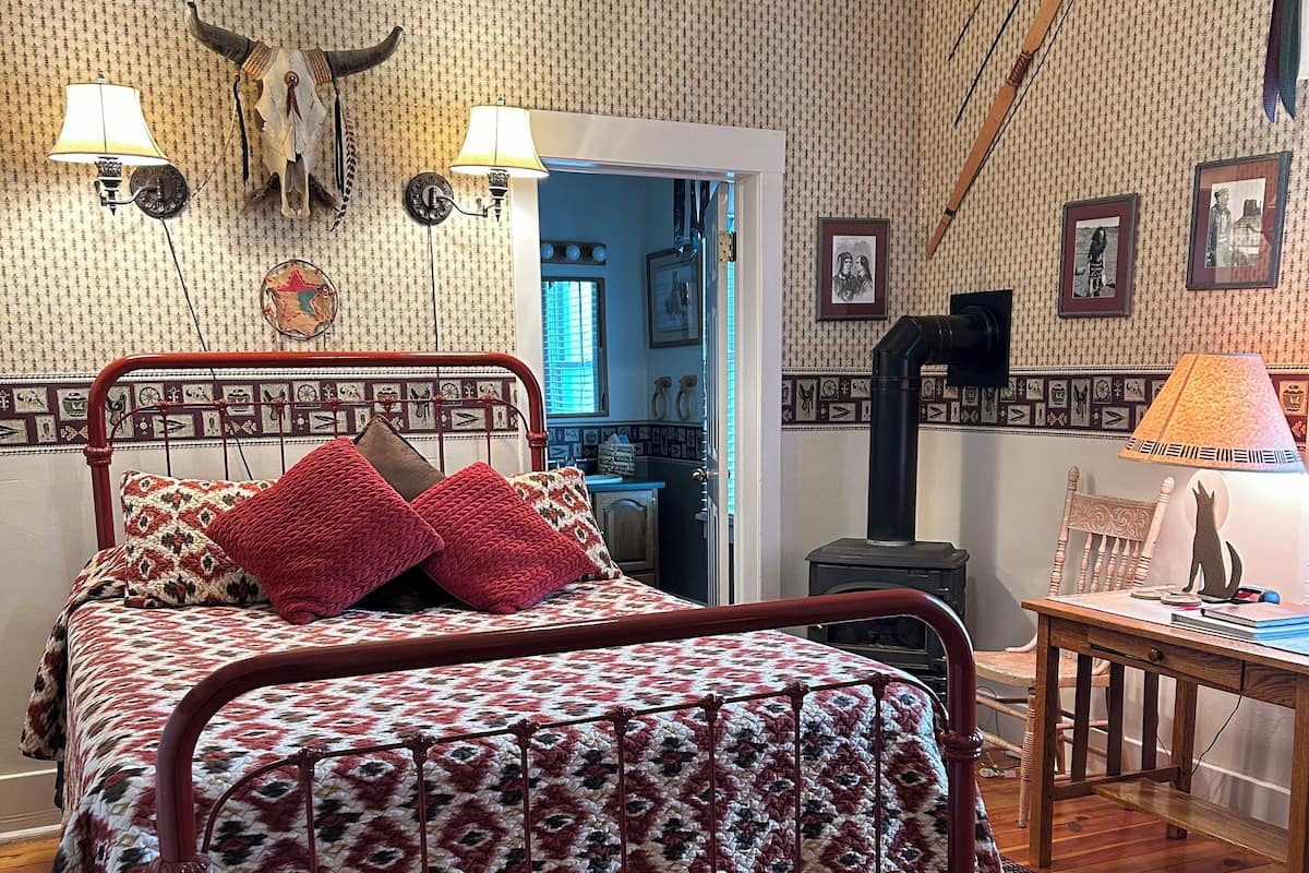 A room with a patterned bed, a wooden floor, and a wall decorated with framed pictures and a cow skull.