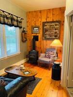 A cozy living room with a wood-burning stove, a comfortable sofa, a small table with a book and a bottle, and a lamp.