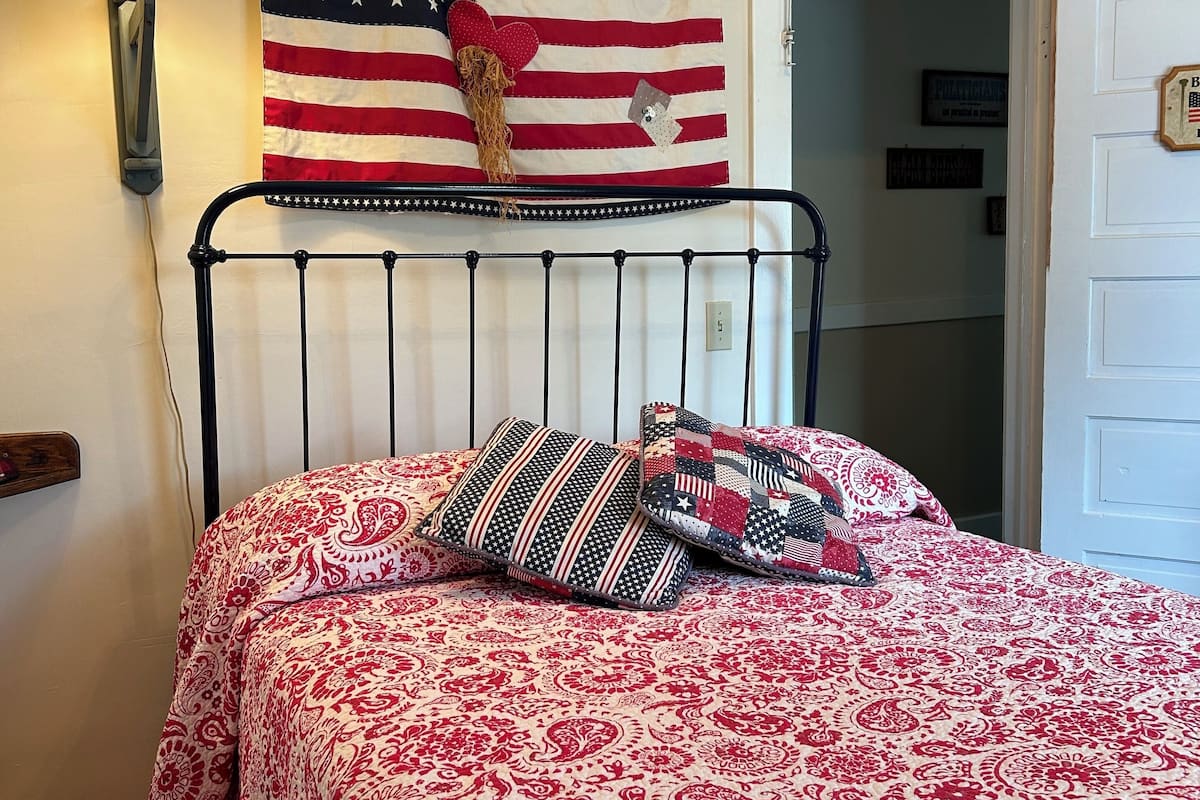 A bed with a red and white patterned bedspread, a black metal headboard, and two pillows with American flag designs.