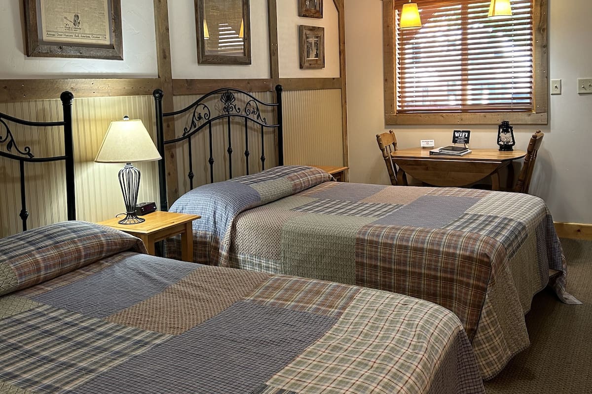 A room with two beds, a table with a sign indicating WiFi, a lamp, and a window with blinds.