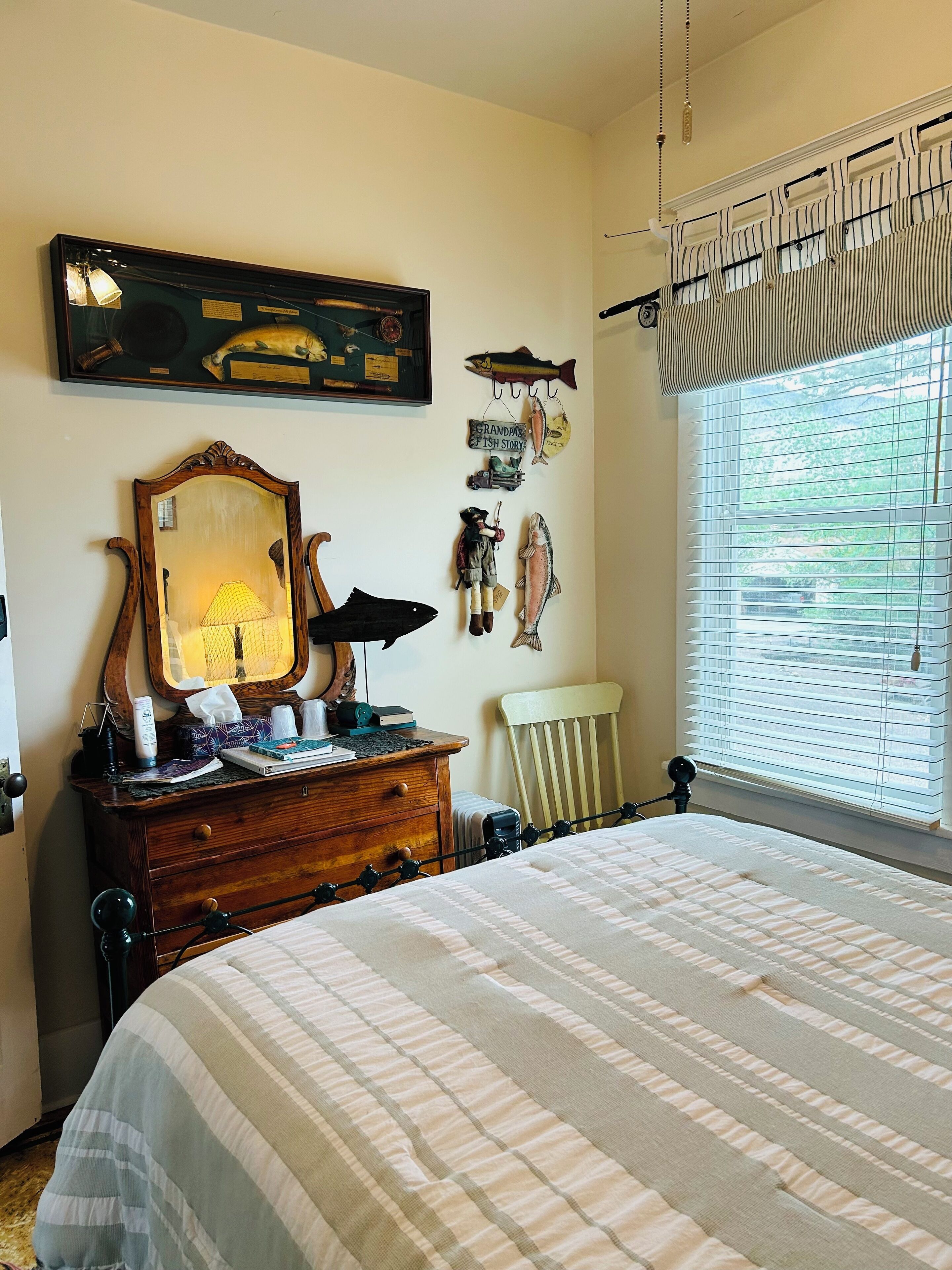 A bedroom with a large bed, a dresser with a mirror, and a window with blinds.