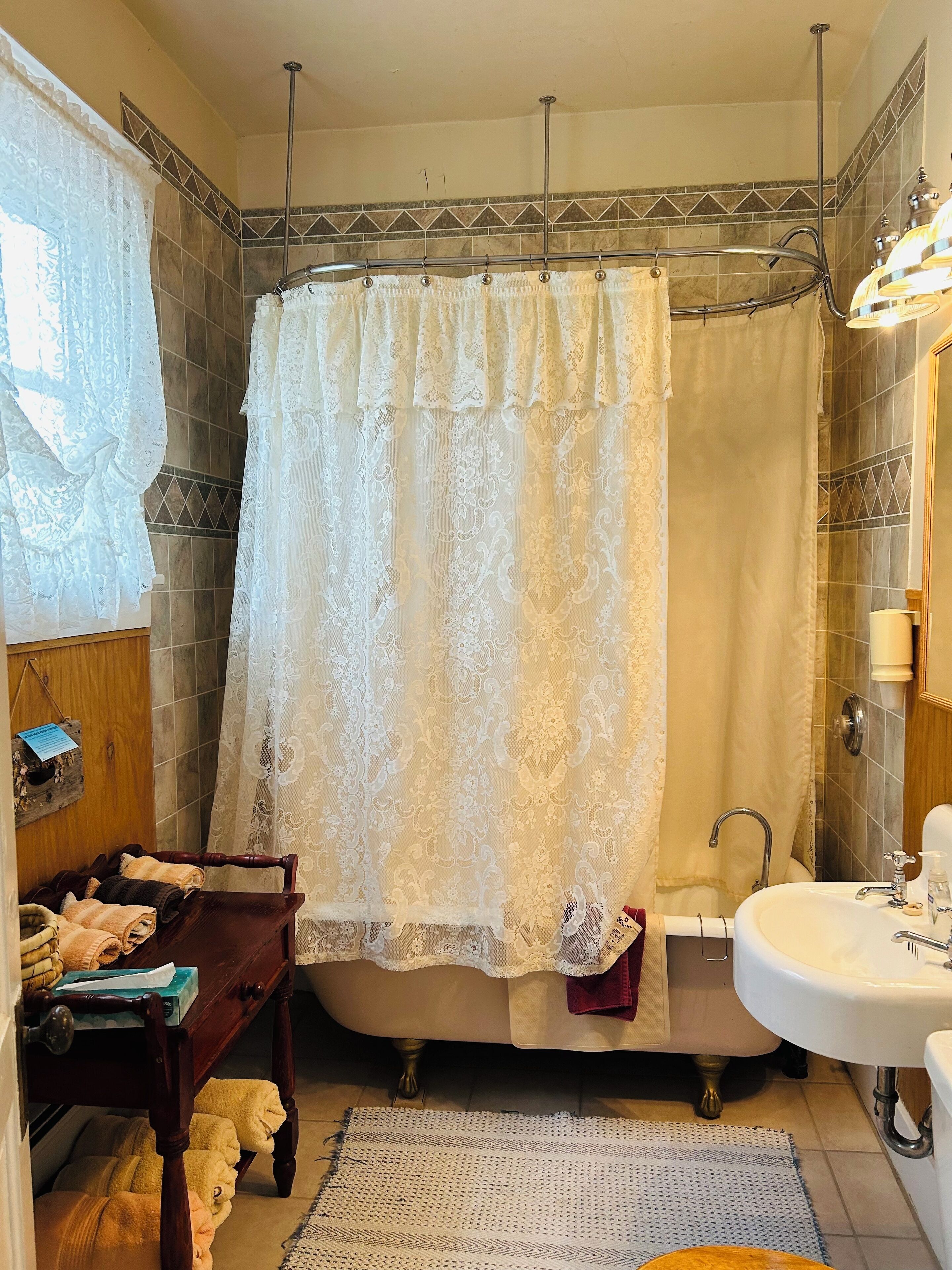 A bathroom with a bathtub, a sink, and a wooden chair with towels.