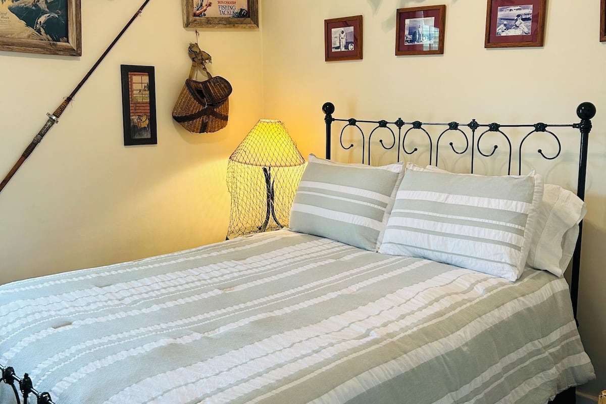 A bedroom with a bed, a lamp, framed pictures, and fishing-related decor.