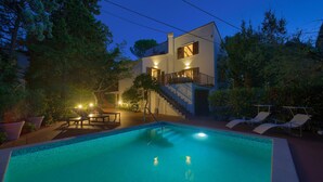 A swimming pool with a staircase leading to a balcony, surrounded by potted plants and outdoor furniture. - Gorgeous home in Malinska (Malinska)