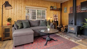 En hyggelig stue med en hjørnesofa, et rundt sofabord, en pejs og trævægge.