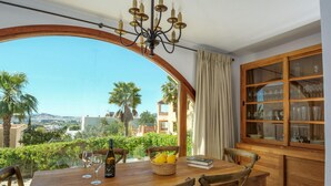 A dining area with a table set for two, a bottle of wine, and a basket of lemons. A large window offers a view of palm trees and buildings. - Awesome home in Ibiza (Ibiza)