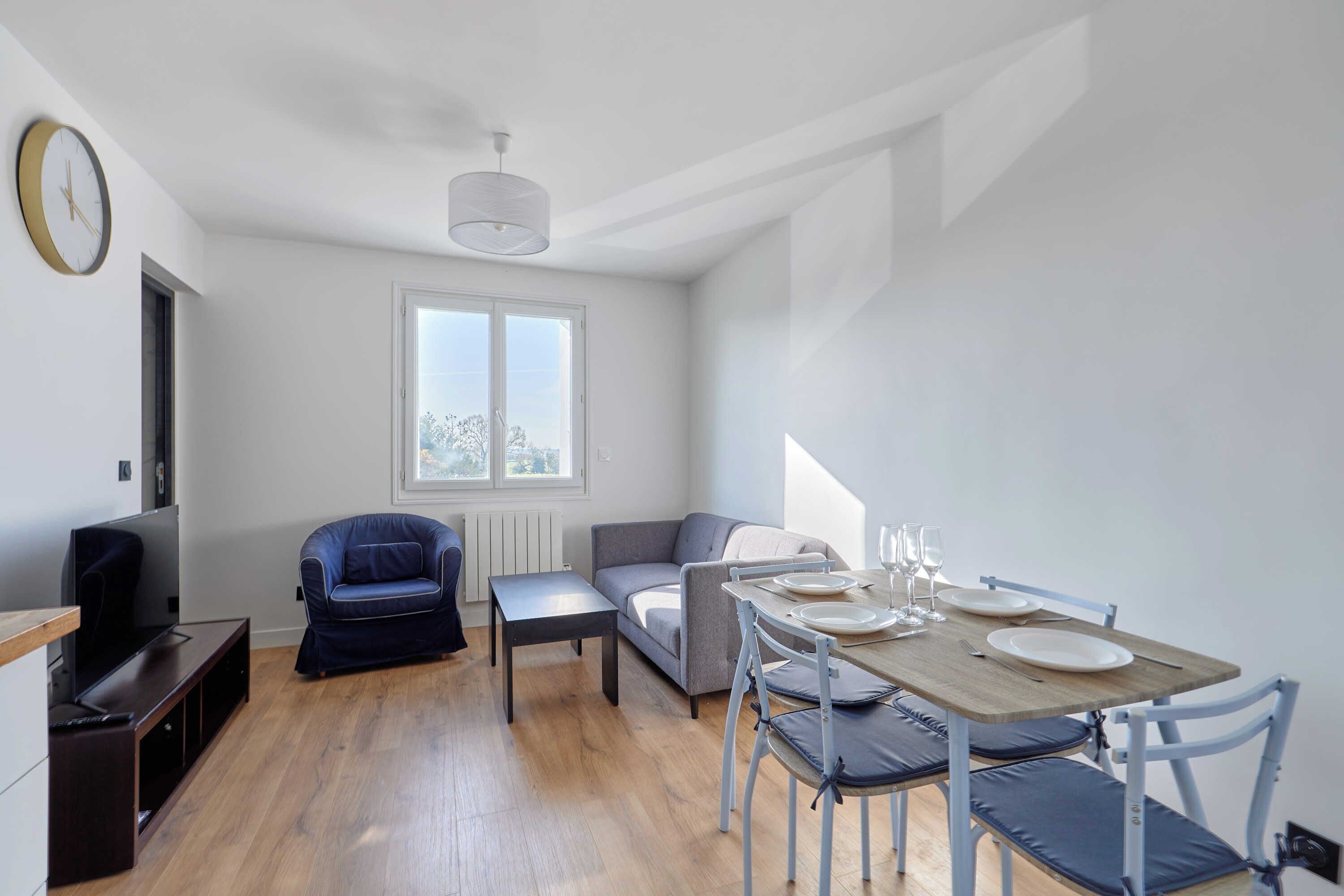 A modern living room with a television, sofa, and dining table set for two.