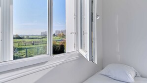 Une pièce dotée d’une grande fenêtre, de murs blancs et d’un seul oreiller blanc sur le lit.